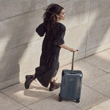 Load image into Gallery viewer, A young woman wearing a black dress and boots, running while dragging her navy blue suitcase.
