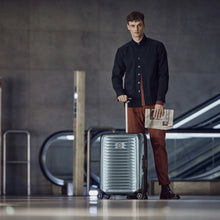 Load image into Gallery viewer, A young man holding a newspaper and his navy blue suitcase.