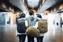 Load image into Gallery viewer, A group of three hug each other to take a picture while carrying their Thule backpacks and a duffle bag.