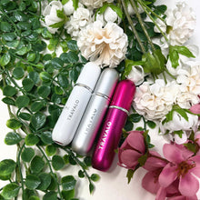 Load image into Gallery viewer, The white, silver, and hot pink perfume atomizers laid on a background of flowers and foliage.