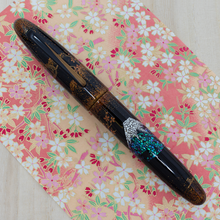 Load image into Gallery viewer, Front view of the fountain pen with the cap on, laid on a print with pink, white and pink cherry blossom flowers.