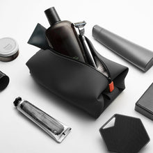Load image into Gallery viewer, Angled view of the black bag filled and surrounded by toiletries.