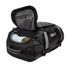 Load image into Gallery viewer, Angled view of the black duffle bag with the main compartment partially unzipped. Clothes and accessories are tucked inside.