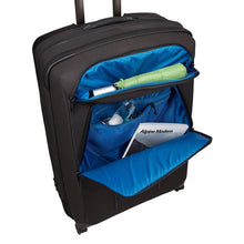 Load image into Gallery viewer, Angled front panel view of the black suitcase showing a set of toiletries and a magazine tucked in the zipper-closing pockets.