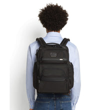 Load image into Gallery viewer, A young man facing back. He carries a black backpack by the shoulder straps.