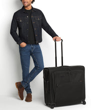 Load image into Gallery viewer, A young man wearing a dark jean jacket holding the wheeled garment bag from the telescopic handle.
