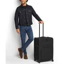 Load image into Gallery viewer, A young man holding the black suitcase by the extended telescopic grab handle.