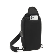 Load image into Gallery viewer, Back panel view of the black sling bag showing a cellphone peeking through the pocket.