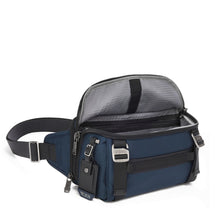 Load image into Gallery viewer, Angled front panel view of the navy blue sling bag showing the main compartment unzipped, and a black tag on the side.
