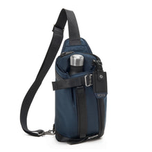 Load image into Gallery viewer, Front panel view of the Navy Blue sling bag with a water bottle shown in the adjustable front pocket. (Water bottle not included).