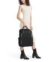 Load image into Gallery viewer, A young woman wearing a beige dress holding the backpack by the top handles.