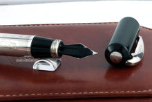 Load image into Gallery viewer, Close up to the nib's feed with the cap set next to it. The top of the cap has a small medal with an engraving.