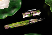 Load image into Gallery viewer, The Visconti Homo Sapiens Lotus Garden Fountain pen with the cap set to the side on a black background with lily pads and white lotus flowers.