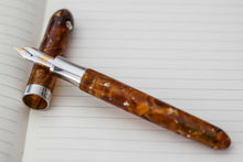 Load image into Gallery viewer, The fountain pen with the nib leaning on the cap. Laid on an notebook with lined paper.