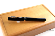 Load image into Gallery viewer, The Fountain Pen leaning on a pen rest on top of the wooden presentation box.