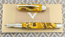 Load image into Gallery viewer, Top view of the Fountain Pen with the cap set next to it. The pen is made of yellow, dark yellow, and white swirls of resin and has palladium plated accents.