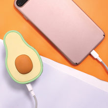Load image into Gallery viewer, Top view of the avocado-shaped power bank connected to a pink cellphone on an orange and white background.