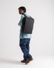 Load image into Gallery viewer, A young man carrying the black backpack on a light gray background.
