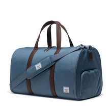 Load image into Gallery viewer, A steel blue duffle bag with brown leather handles and a brown stripe lining. The adjustable shoulder strap is set across the front.
