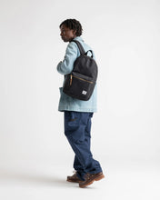 Load image into Gallery viewer, A young man facing left while carrying a black settlement backpack. 
