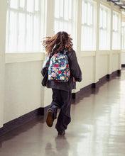 Load image into Gallery viewer, A model walking down a windowed hallway wearing the floral backpack.
