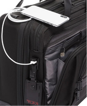 Load image into Gallery viewer, Angled close up of the wheeled laptop case. The fron panel compartment is unzipped, and a phone is connected to the USB port. 
