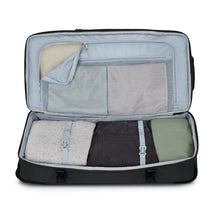 Load image into Gallery viewer, Interior view of the black duffle bag's bottom compartment. A set of clothes is folded inside and in the zipper-closing pocket.
