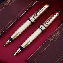 Load image into Gallery viewer, Front view of the mechanical pencil and ballpoint pen. on the presentation box with the included booklets. They are gold-plated with engraved decorations. Black resin accents are placed at the top, middle and grip sections. 
