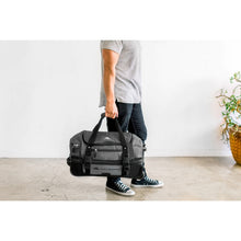 Load image into Gallery viewer, Person carrying the black High Sierra wheeled duffel bag by its webbed handles.
