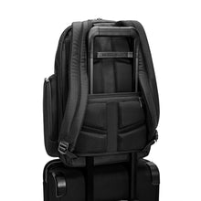 Load image into Gallery viewer, Back panel view of the black backpack with the attachment feature holding it to a suitcase's handle. 

