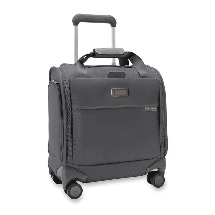 Angled front view of the steel gray baseline cabin spinner. It features a telescopic handle, a set of carrying handles at the top, and 4 spinner wheels. The leather monogram label can be embossed with up to 3 characters.