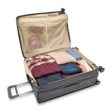 Load image into Gallery viewer, The suitcase laid down with the main compartment opened, and filled with folded clothes. 

