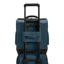 Load image into Gallery viewer, Back panel view of the ocean blue underseat cabin bag with the attachment strap holding it onto a suitcase. 
