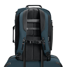 Load image into Gallery viewer, Back panel view of the ocean blue backpack with the attachment strap holding it on to the extended handle of a suitcase. 
