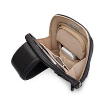 Load image into Gallery viewer, Angled interior view of the black sling bag with electronics tucked into the organization pockets. 

