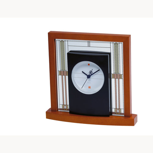 Front angled view of the table clock. The clock face is round and placed within a black frame. This frame is inserted into a wooden frame with a decorated mineral glass panel.