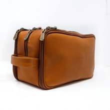 Load image into Gallery viewer, Angled View of the tan leather shaving kit bag. Three zip compartments and Matching Leather handle grip are set on the left side.
