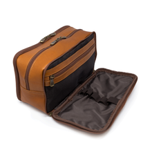 Load image into Gallery viewer, Angled view of the tan leather shaving kit bag with the front compartment unzipped. It features organizing straps and an inner  zipper-closing pocket.
