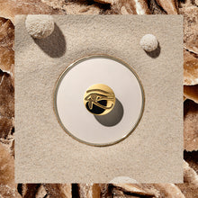 Load image into Gallery viewer, The eye of Horus medal arranged on a stylized background with sand. 
