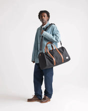 Load image into Gallery viewer, A young man carrying the duffle bag on his shoulder on a light gray background.
