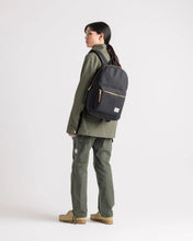 Load image into Gallery viewer, A young woman dressed in green carrying the black settlement backpack on her shoulder.
