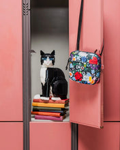 Load image into Gallery viewer, The floral crossbody bag hanging from the door of an opened pink locker with books and a Lego brick cat.
