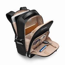 Load image into Gallery viewer, Angled view of the black backpack with all the compartments opened. A laptop and tablet, notebook, keys, pen, and passport are organized inside different pockets.
