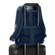 Load image into Gallery viewer, Back panel view of the navy blue backpack. The horizontal attachment strap is holding it on to the extended handle of a suitcase.
