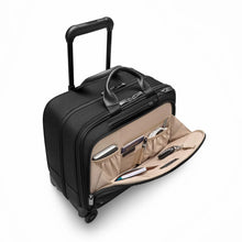 Load image into Gallery viewer, Angled view of the black spinner brief with the front panel pocket unzipped. A battery bank, passport, pen, USB cable and keys on a key sling are organized in the compartments.
