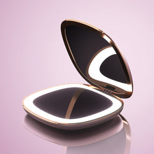 Load image into Gallery viewer, Angled view of the pink pocket mirror, opened and with the light on. Set on a pink background.
