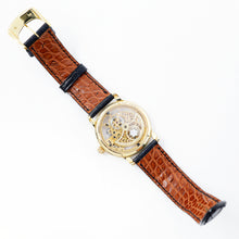 Load image into Gallery viewer, Back panel view of the golden mechanical watch. The strap is made of textured tan leather with black stitching on this side. 
