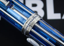 Load image into Gallery viewer, A close-up of the blue and silver solid gold pen with a decorative silver band set with small blue stones, shown against a dark background with blurred white lettering.

