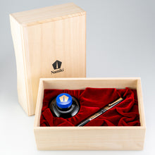 Load image into Gallery viewer, View of the Fountain Pen on its wooden presentation box. The lid has the black Namiki Logo placed in the center. The inside of the box holds the pen and the ink, each in a compartment lined with a soft vibrant red fabric. 
