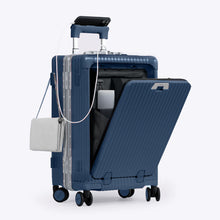 Load image into Gallery viewer, Angled front view of the blue colored carry-on with the front panel opened. It is arranged with a charging cellphone, a small purse, and a laptop in its compartment. 
